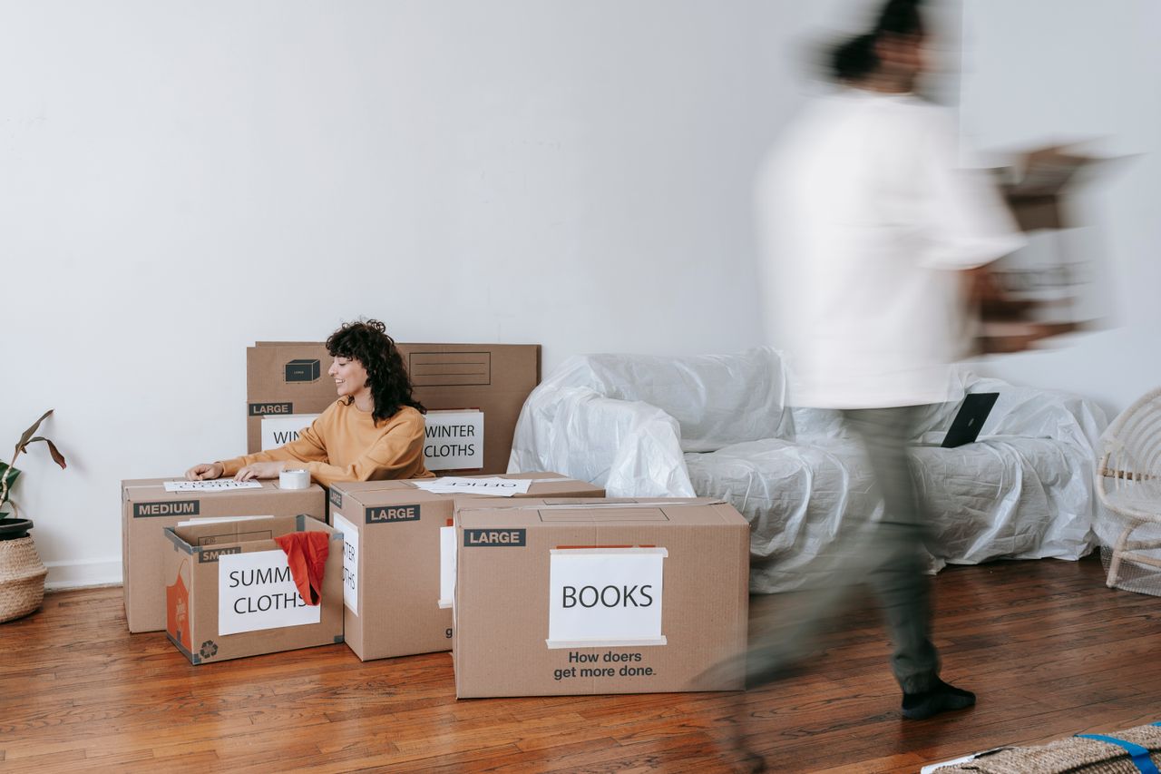 Un couple range des cartons étiquetés dans un salon épuré, en train de se préparer pour le jour du déménagement.